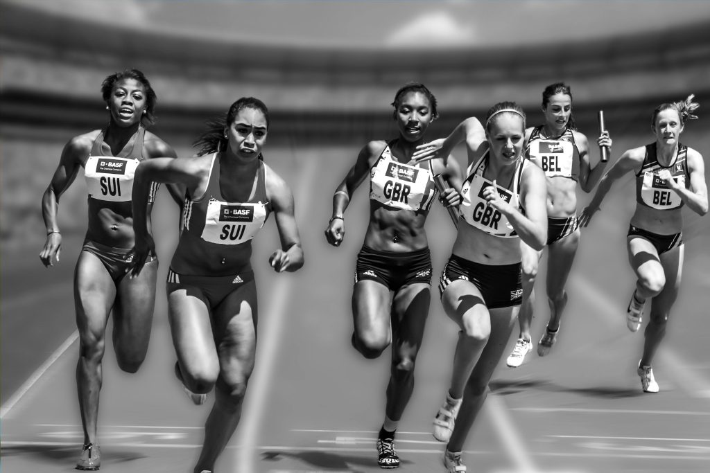 Atletas femeninas corriendo en una carrera de relevos, vistiendo uniformes que representan a sus países: Suiza, Gran Bretaña y Bélgica.