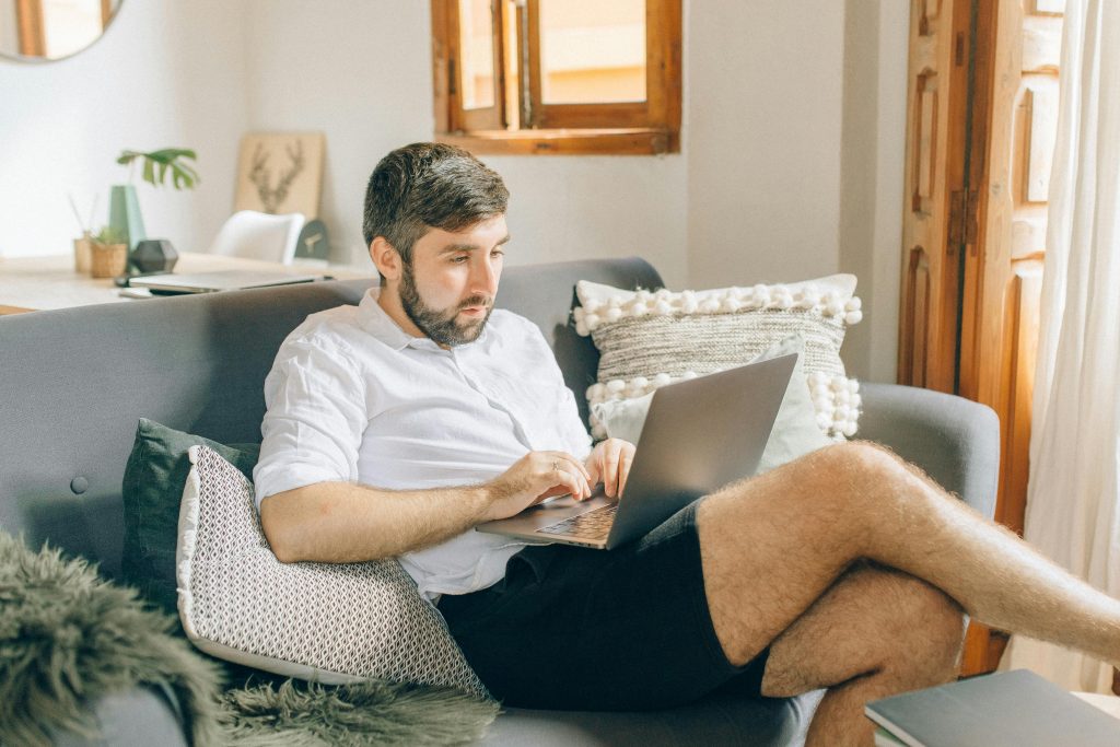 Hombre sentado en un sofá trabajando en su portátil desde casa, mostrando una actitud cómoda y relajada en un entorno doméstico.